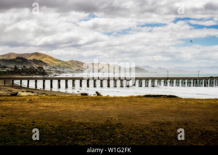 Pier ins Meer entends in der kalifornischen Küste Landschaft Bild unter Wolken und blauer Himmel mit einem seevogel Fliegen in Abstand. Stockfoto