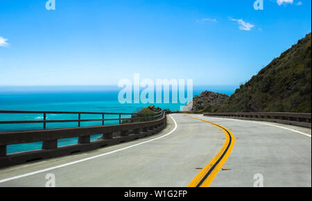 Straße führt entlang der Küste von Kalifornien auf der Autobahn 1 mit geschwungenen Bürgersteig und Leitplanken, die über helle blaue Wasser. Stockfoto