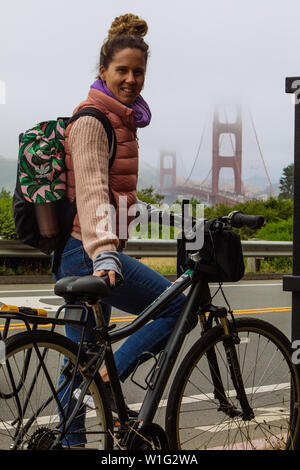 Frau mittleren Alters posiert mit Fahrrad mit nebliger Golden Gate Bridge in San Francisco, Kalifornien, USA Stockfoto