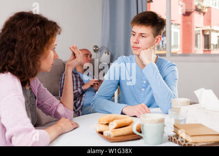 Portrait des gestörten Teenager Jungen und seine Mutter ihn schimpfen, während Vater sitzt auf einem Sofa Stockfoto