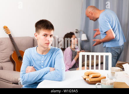 Portrait von umgekippt Teenager sitzen am Tisch, während die Eltern zu Hause Streit Stockfoto