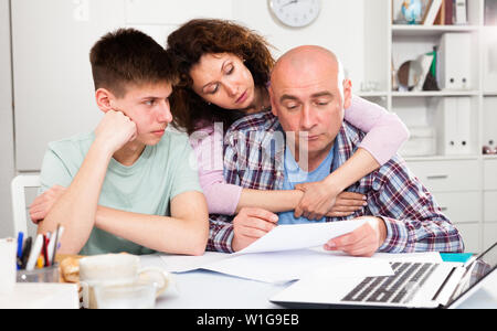 Junger Mann mit seiner Frau und seinen jüngeren Sohn Lesen von Dokumenten zu Hause Tabelle Stockfoto