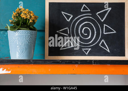 Kreative Bild von gelben Blumen im Topf mit blauen Hintergrund Mit bebilderter Beratung zur Pflege der Pflanzen mit Kreide auf einer Tafel. Stockfoto