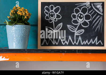 Kreative Bild von gelben Blumen im Topf mit blauen Hintergrund Mit bebilderter Beratung zur Pflege der Pflanzen mit Kreide auf einer Tafel. Stockfoto