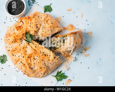 Griechische Torte backen spanakopita auf weißem Papier über blauen Hintergrund. Ideen und Rezepte für vegetarische oder vegane Spanakopita Spinatkuchen von fillo Blätterteig in Scheiben geschnitten. Kopieren Sie Platz. Top View oder flach. Stockfoto