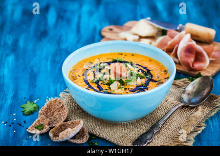 Kürbis creme Suppe Schüssel, serviert mit Sesam, Schinken, Parmesan, Olivenöl, Balsamico und Kräuter Stockfoto
