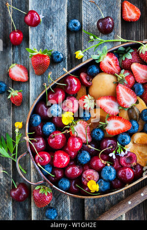 Frische reife Sommer Beeren und Früchten (Kirsche, Erdbeere, Heidelbeere, Aprikosen) auf rustikalen Holzmöbeln Hintergrund, Ansicht von oben Stockfoto
