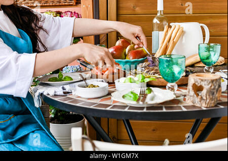 Ein Mädchen mit einem Topf mit gebratenen Garnelen sitzt am Tisch. Viele verschiedene Lebensmittel. Serviert. Gemütliches Heim Stockfoto