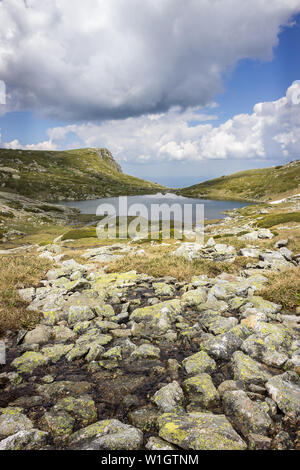 Vordergrund Felsen bedeckt durch gelbe Moos, blauer See, felsigen Gipfel und erstaunliche sonnenbeschienenen Landschaft von Rila Gebirge in Bulgarien Stockfoto