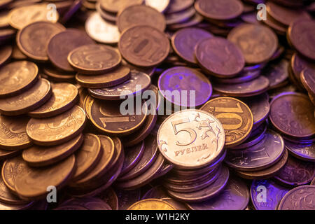 Eine Handvoll Gold- und Silbermünzen in einem violetten Licht. eine Handvoll Münzen der Rubel im dunklen Licht. Stockfoto