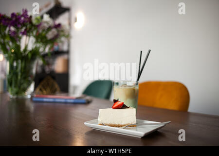 Lecker lecker Kuchen mit Erdbeeren und kaltem Kaffee Frappe mit Eis. Cafe innen im Hintergrund. Stockfoto
