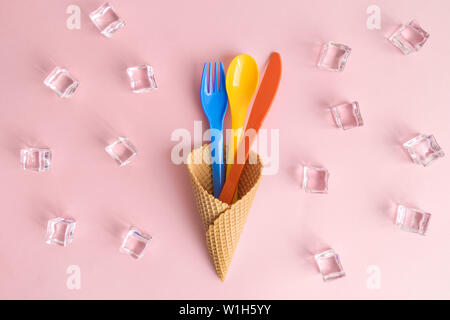 Flach mit bunten Kunststoff Besteck in Eis mit Eiswürfeln gegen Pastell rosa Hintergrund minimal kreative Essen und Trinken Konzept. Stockfoto