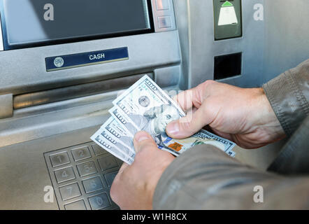 Die Hände eines Menschen sind holding US Dollar Banknoten auf dem Hintergrund der ATM. Stockfoto