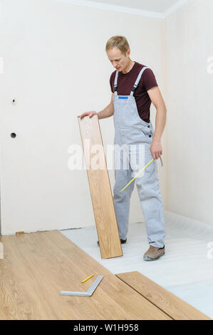 Installation eines Laminats Diele. Der Arbeitnehmer hält ein Laminat floorboard für die Verlegung auf dem Boden. Stockfoto