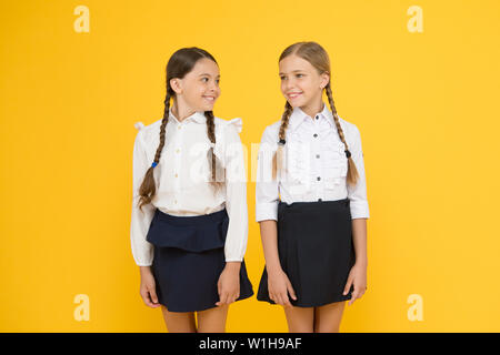 Freundliche Schüler. kleinen Mädchen auf gelben Hintergrund. Freundschaft und Schwesternschaft. beste Freunde. Kid formale Art und Weise. Ausbildung im Ausland. smart suchen Kinder. Schule Freunde. glückliche Kinder in Uniform. Stockfoto