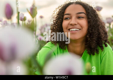 Gemischte Rasse schöne Afrikanische Amerikanische biracial Mädchen Teenager weibliche junge Frau mit grünem T-Shirt in Bereich der rosa Blumen Mohnblumen bei Sonnenuntergang oder su Stockfoto