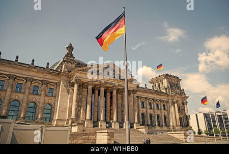 Deutsche Fahnen im Wind am berühmten Reichstag, Sitz des deutschen Parlaments Deutscher Bundestag, an einem sonnigen Tag mit blauen Himmel und Wolken, zentrale Berlin Mitte, Deutschland Stockfoto