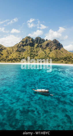 Luxus Kreuzfahrt Yacht segeln über Korallenriff mit erstaunlichen tropischen Strand und Blick auf die Berge. Luftaufnahme. Insel Padar, Komodo Indonesien. 16:9 für Telefon Stockfoto