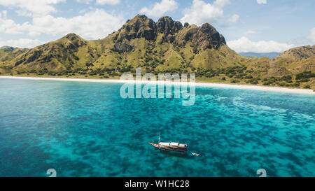 Luxus Kreuzfahrt Yacht segeln über Korallenriff mit erstaunlichen tropischen Strand und Blick auf die Berge. Luftaufnahme. Insel Padar, Komodo Indonesien. Stockfoto