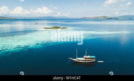 Luxus Kreuzfahrt Yacht segeln in der Nähe von Coral Reef Atoll Insel mit fantastischen weissen tropischen Strand und Berge am Horizont. Luftaufnahme. Luxus marine Reisen