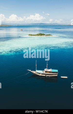 Luxus Kreuzfahrt Yacht segeln in der Nähe von Coral Reef Atoll Insel mit fantastischen weissen tropischen Strand und Berge am Horizont. Luftaufnahme. Luxus marine Reisen