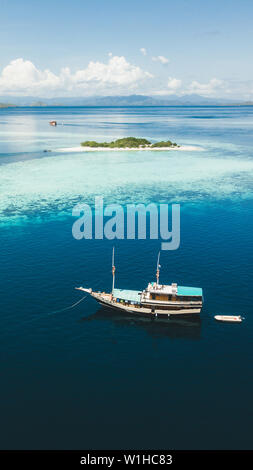 Luxus Kreuzfahrt Yacht segeln in der Nähe von Coral Reef Atoll Insel mit fantastischen weissen tropischen Strand und Berge am Horizont. Luftaufnahme. 16:9 Der Bildschirm "Telefon" Stockfoto