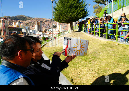 La Paz, Bolivien 2. Juli 2019: Eine Frau zeigt einen Mann das Bild der Sonne innerhalb einer Lochblende Projektor aus einer Cornflakes-packung gemacht während eines partiellen Sonnenfinsternis eine Sonnenfinsternis beobachten Ereignis in der Nähe des Stadtzentrums. In La Paz der Eclipse dauerte ca. 2 Stunden, 10 Minuten mit über 55% Abdeckung maximal. Stockfoto