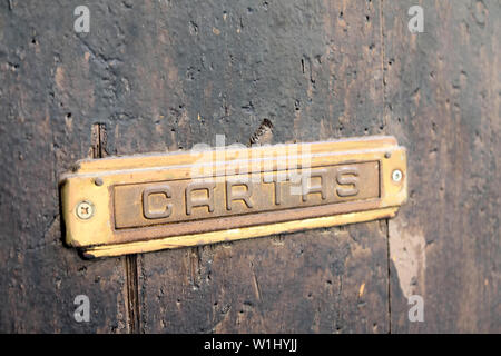 Abgewinkelte Seitenansicht eines verwitterten Messing Briefkasten mit dem Wort "cartas' auf seine Klappe in einem alten Pockennarbig braunes Holz Tür geprägt; Granada, Spanien. Stockfoto