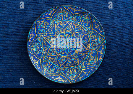 Dekorative Keramik Platte mit blauen und goldenen Farben, lackiert Platte auf dem Hintergrund der blauen Stoff, aus der Nähe. Dekoratives Porzellan Teller bemalt wit Stockfoto