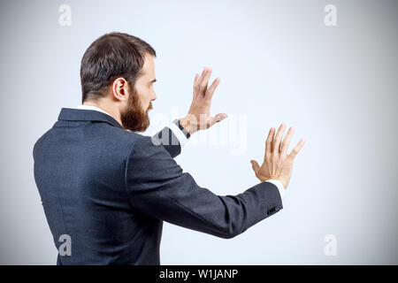 Geschäftsmann in Anzug zeigt ausgestreckte Hand withspread Finger. Über grauen Hintergrund. Ansicht von hinten. Stockfoto