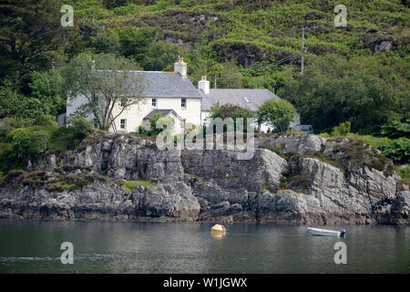 Croft Haus auf Water's Edge von Loch in Schottland. Ein Boot ist in der Nähe der felsigen Ufer vertäut. Stockfoto