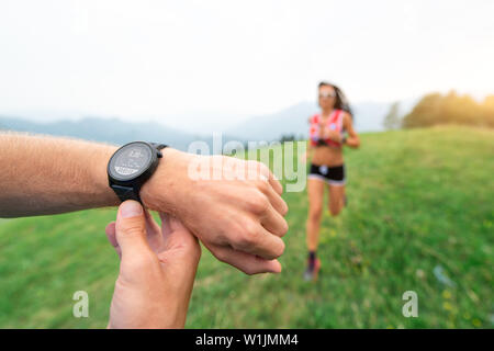 Athletischer Trainer hält die Stoppuhr während des Trainings ein Mädchen läuft in der Natur Stockfoto