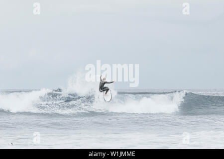 Pro Surfer Reiten eine kleine Welle im Beach in Kalifornien an einem bewölkten Tag Stockfoto