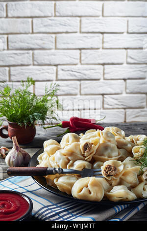 Hausgemachte heiße Teigtaschen mit Hackfleisch Füllung auf eine schwarze Platte mit einer Mauer diente, frischer Dill und Tomatensauce in eine Schüssel im Hintergrund, ve Stockfoto
