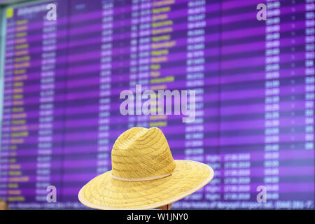 Ein Mann in einem Strohhut steht vor einer unscharfen Informationen Board für An- und Abflüge. Informationen stehen am Flughafen, Bahnhof Stockfoto