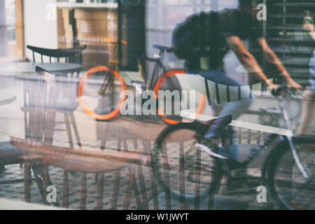 Abstrakte cafe Reality Game mit Stühlen und Biker Reflexionen in einer Glasvitrine auf einer Straße von Riga Stockfoto
