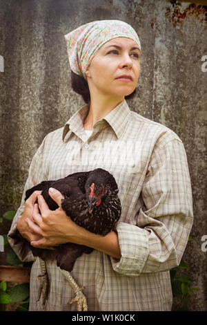 Frau Bauer in der Kleidung der Männer, mit einem schwarzen Huhn in ihre Hände in den ländlichen Szene. Stockfoto
