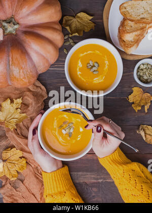 Woman's Hände, die Tabelle sppoon in der Nähe der Schüssel köstliche selbstgemachte Kürbissuppe mit Creme auf dem Holztisch, Ansicht von oben Stockfoto