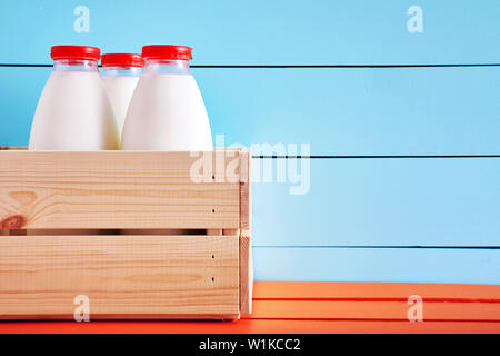 Milch Flaschen in Holzkiste auf hölzernen Küchentisch mit blauem Holz- Hintergrund. Nahaufnahme mit Kopie Raum Stockfoto