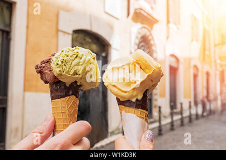 Zwei Hände close-up Holding Kegel mit italienisches Eis gelato auf dem Hintergrund von Rom streeet. Europäische Ferienhäuser Konzept Stockfoto