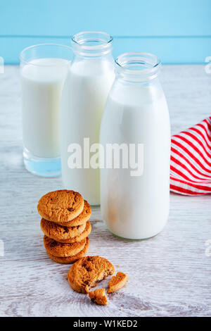 Zwei Flaschen Milch, Chocolate Chip Cookies und ein Glas voll Milch auf Holztisch mit blauem Holz- Hintergrund. Stockfoto