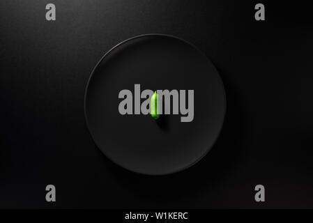 Ein mini Gurke in schwarz Platte auf Moody schwarzen Hintergrund serviert. Ansicht von oben. Gesunde Ernährung Konzept. Stockfoto