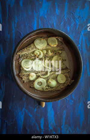 Makrele mit Zwiebeln gebacken in Lehm Topf auf blauem Hintergrund Stockfoto