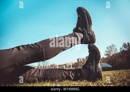 Die Beine des Athleten in Leggings und Sneakers, auf dem Boden liegend auf der Wiese in der Nähe. gekreuzten Beinen. Ausbildung auf dem freien. Warm-up, Stretching. Stockfoto