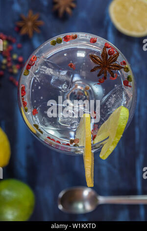 Gin Tonic in einem Glas Schale mit Schichten aus Kalk und Zitrone, rosa Pfeffer und Anis auf einem blauen und schwarzen rustikalen Hintergrund Stockfoto