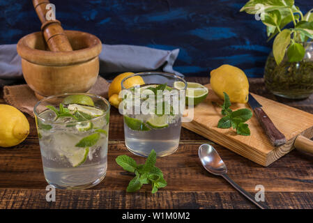 Mojito Cocktail mit den zutaten Pfefferminze, Limette und Zitrone auf einem Holztisch und blauer Hintergrund Stockfoto