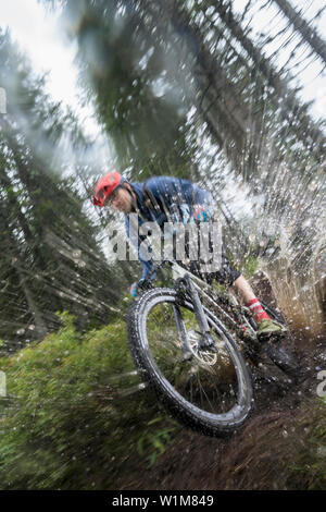 Biker Fahrten durch eine Pfütze im Wald an regnerischen Tag, Saalfelden, Tirol, Österreich Stockfoto