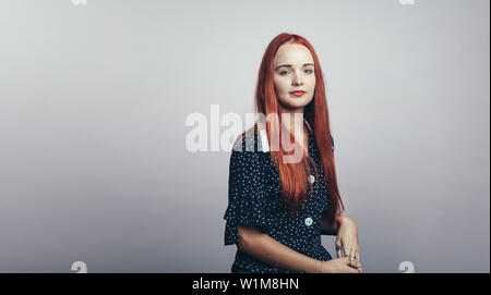 Porträt der jungen Frau an der Kamera schaut. Frau mit langen rotbraunen Haare vor grauem Hintergrund sitzen. Stockfoto