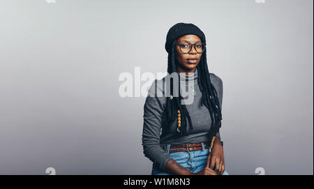 Afrikanische Frau auf grauem Hintergrund. Portrait von afrikanischen Frauen mit langen dreadlocks auf Kamera schaut. Stockfoto