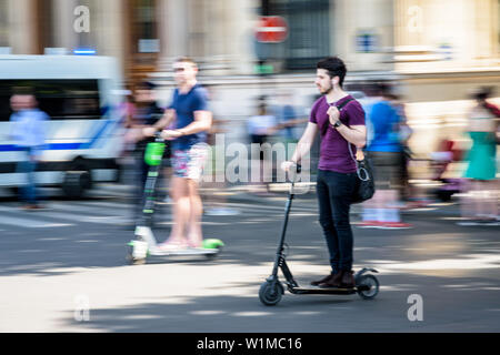 Ein junger Mann fährt mit einer Hand einen Elektroroller bei hoher Geschwindigkeit, Überholen eines anderen Mannes auf einem elektrischen scooter in den Straßen von Paris, Frankreich. Stockfoto